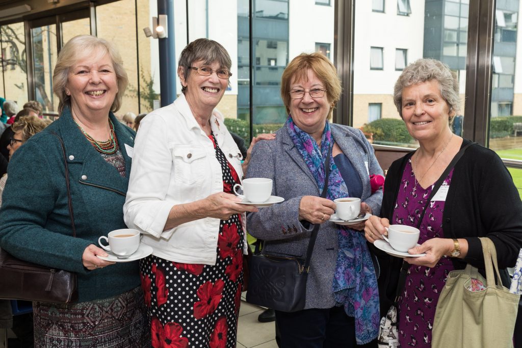 Four smiling older ladies holding cups of tea.
