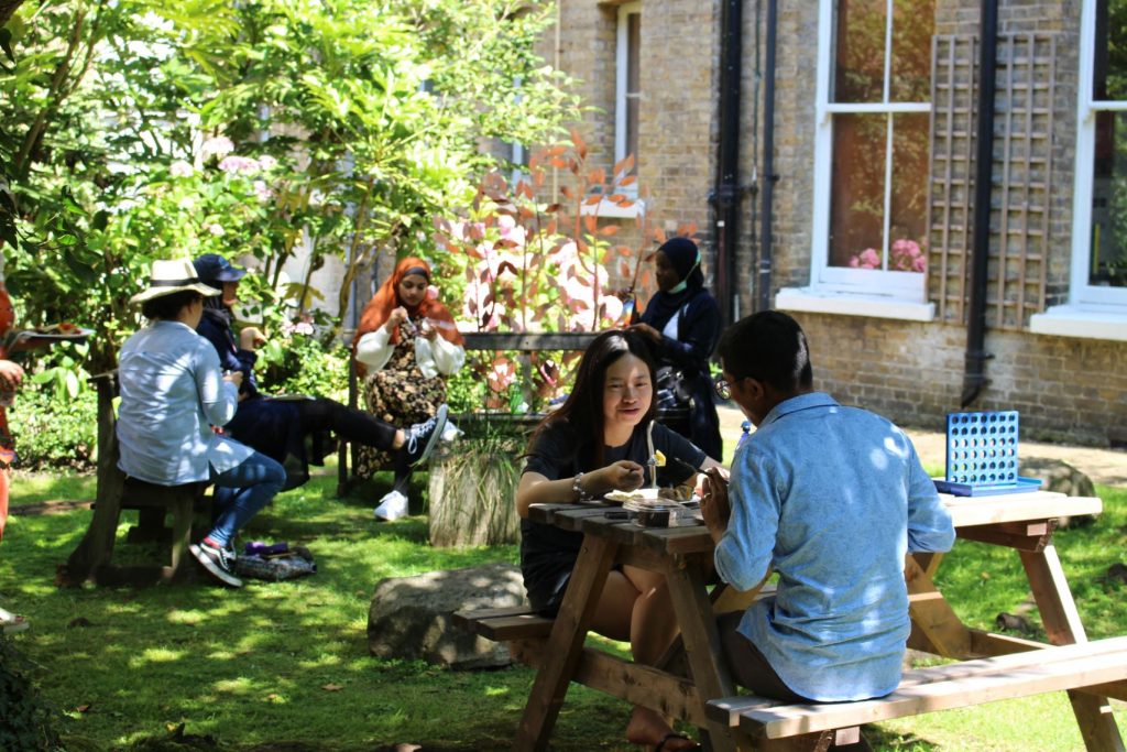 Six people sitting on benches in pairs in a sunny garden.